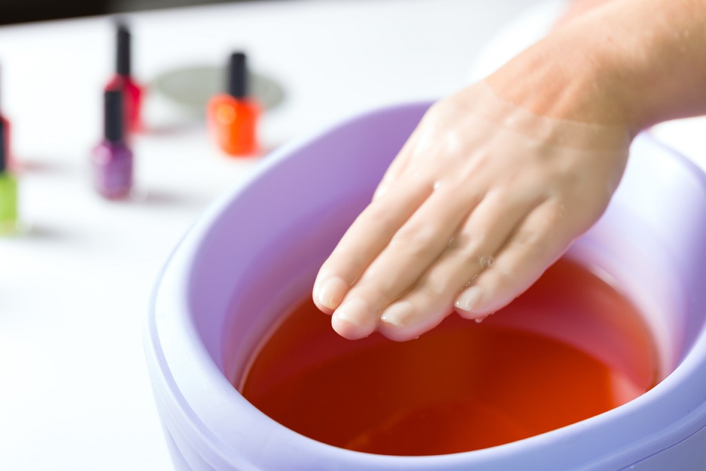Woman in a nail salon receiving a manicure, she is bathing her hands in paraffin or wax