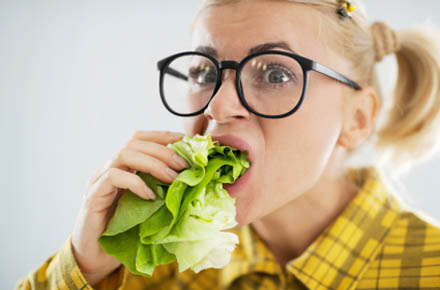 Blonde woman with the scary expression on her face while eating cabbage leaf.