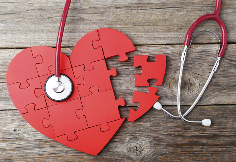 Red puzzle heart with stethoscope on grey wooden background