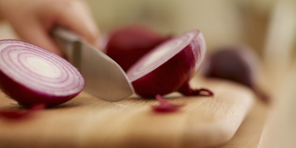 Knife chopping red onion on cutting board
