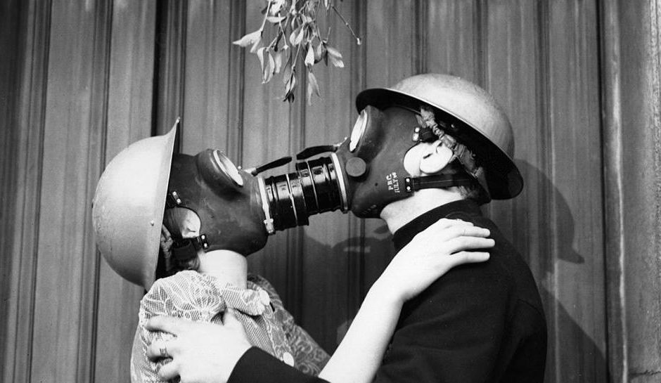 A couple kissing under the mistletoe, wearing gas masks. (Photo by Fox Photos/Getty Images)