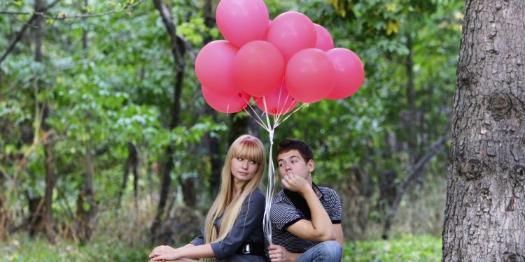 young couple with red balloons on natural background