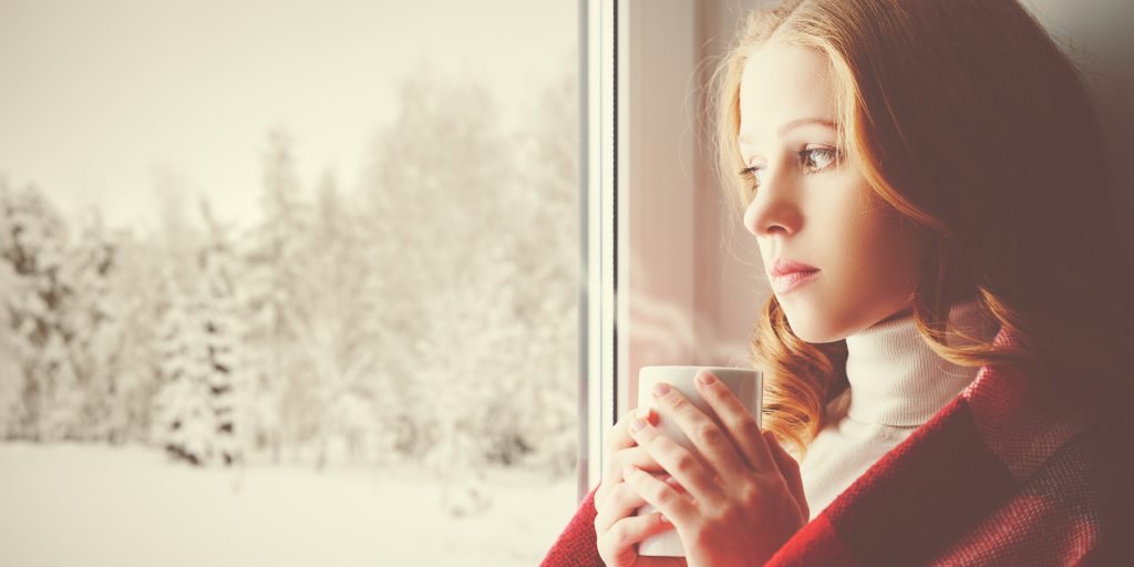 Pensive sad girl with a warming drink looking out window
