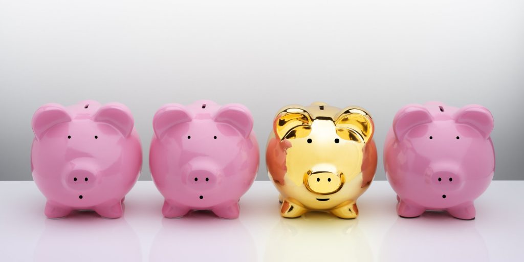 One gold piggy bank outshines the three pink piggy banks standing in a line besides it