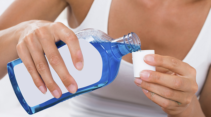 Close-up Of Woman Hands Pouring Mouthwash Into Bottle Cap